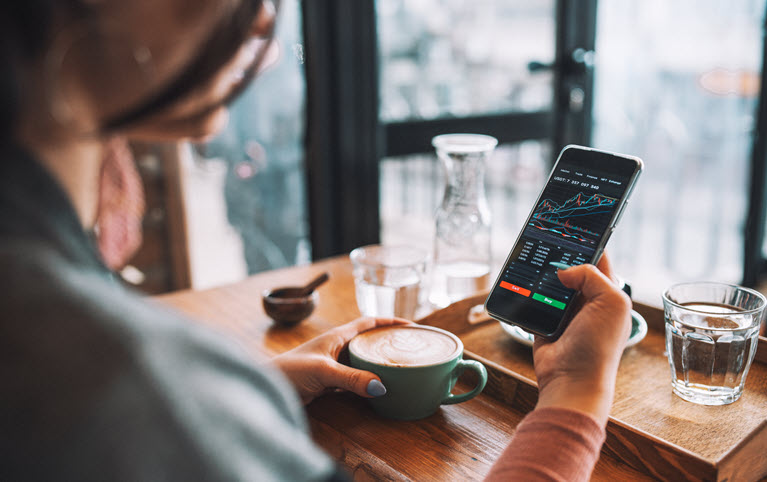 Woman holding a coffee, looking at the stock market on her cellphone.