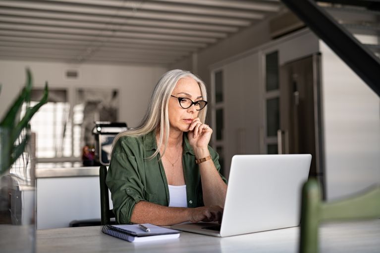 Focused older woman at home using laptop.