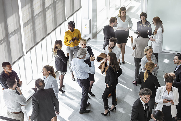 Diverse group of business professionals conversing and networking in a sunlit office hallway.
