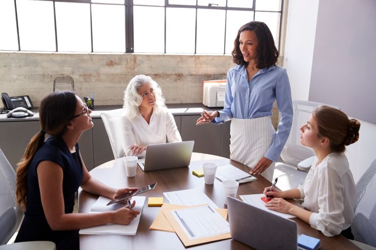 four women sitting around a round table in the office having a meeting