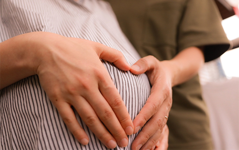 A couple touching the top of their pregnant belly, showing a heart sign with both their hands. 