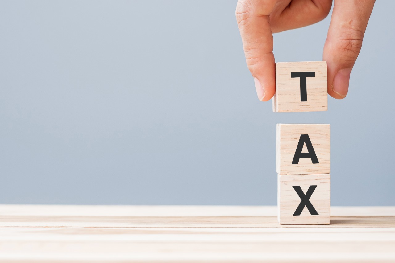 An image on a hand pulling wooden boxes with letters to form the word Tax.