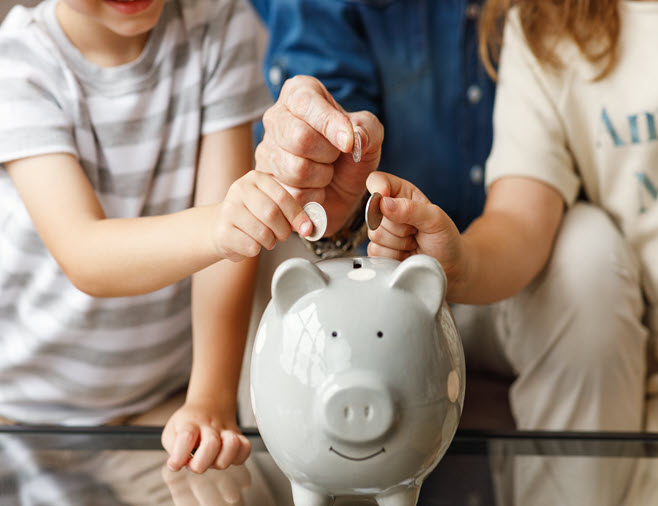  three hands belonging to a mother, a child and a father, who are making a deposit of coins in a piggy bank