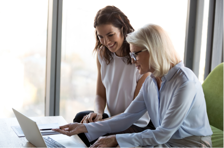 Two women in front of a desk with a portable computer on it.