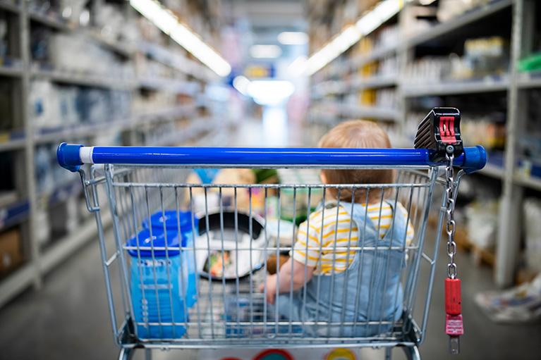 young child sitting inside a grocery cart in a grocery store aisle