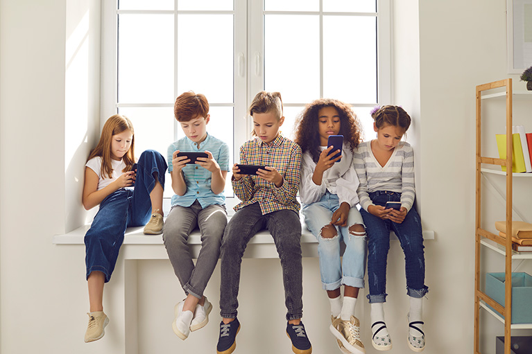 a group of teenagers sitting in front of a window all looking at their cell phone