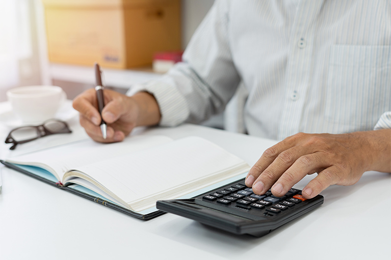 man filling in a leger with pen and working on calculator