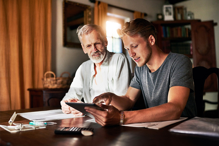 Older father with his young adult son sitting at the table reviewing finances