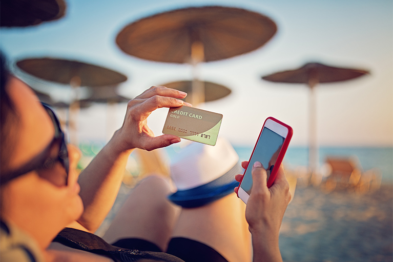 woman lying on lounger on a beach holding her credit card and phone