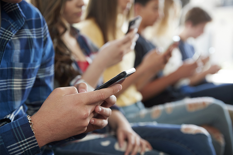 teens sitting in a row all looking at their phones