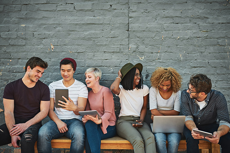 diverse group of millennials social networking outside sitting on a bench 