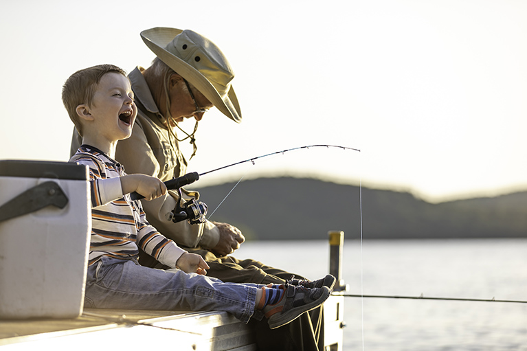 older man (grandfather) and young boy sitting on a dock fishing