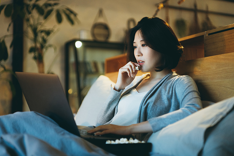 asian girl watching a movie on her laptop shitting on the couch