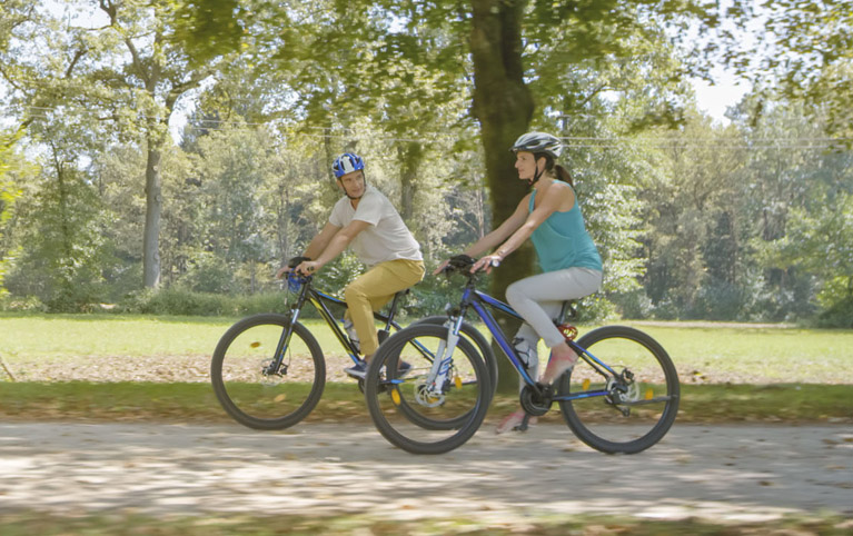 a male and female riding bicycles through a park