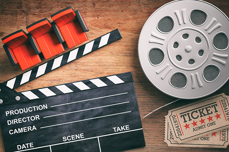 image film reel, tickets from movie, directors board and 3 theatre chairs arranged on a wood background