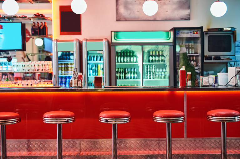 image of a counter at a diner with the red stools and refrigerators behind the counter showing drinks