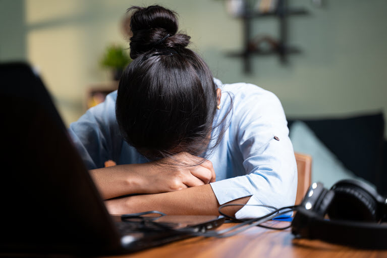 a young woman sitting at a desk with her head down on her hands