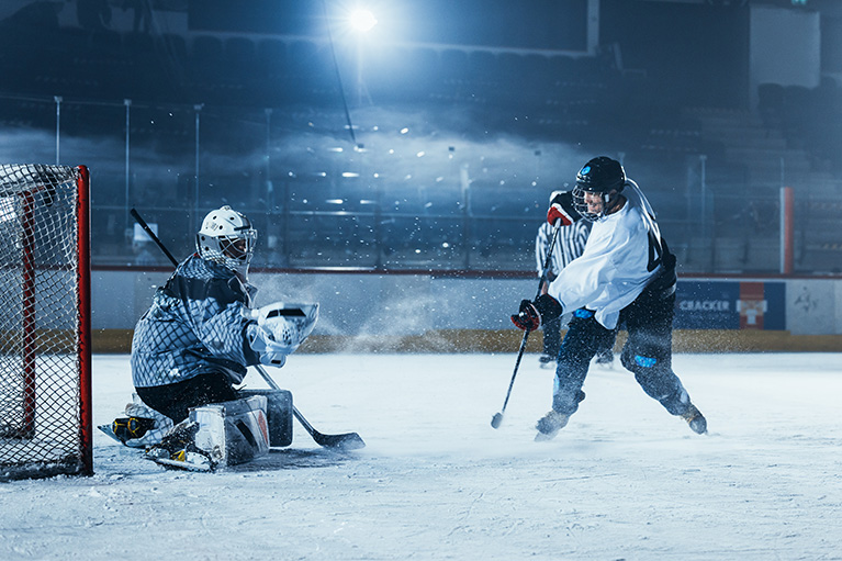 hockey goalie in net with player trying to score in a rink