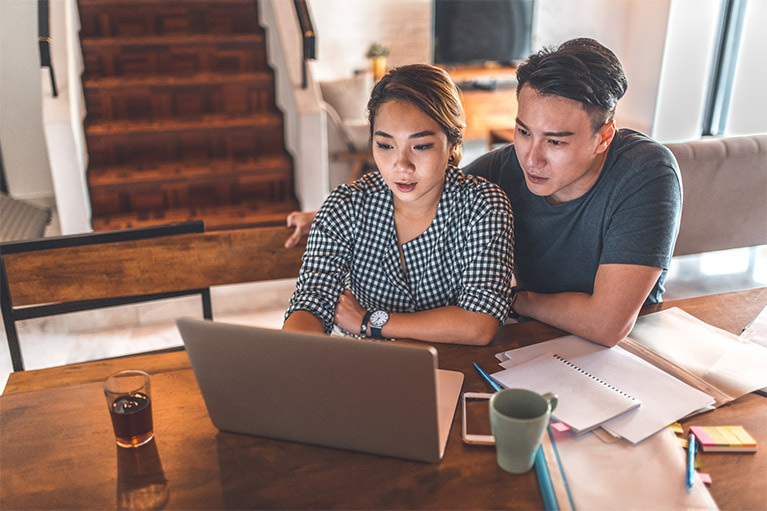 young couple sitting at the dining room table looking at their laptop together