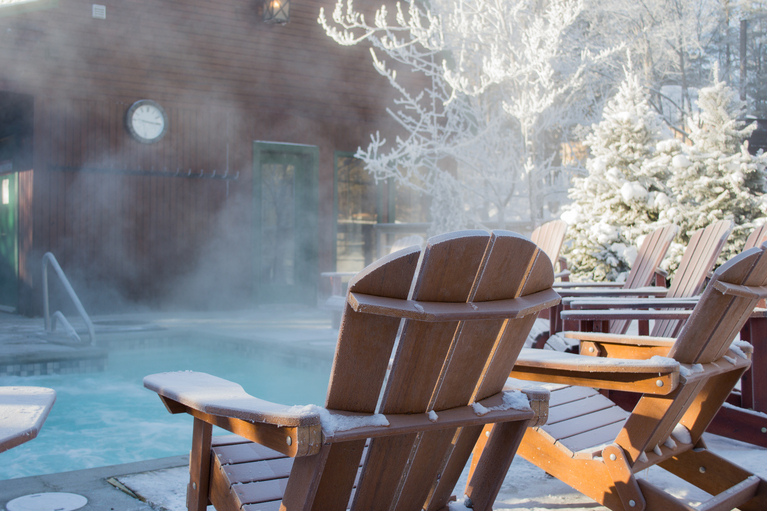 deck chairs facing a pool in the winter with steam coming off the water