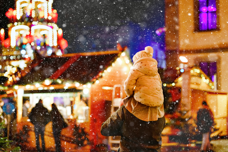 child on parents shoulder walking outside in a Christmas market