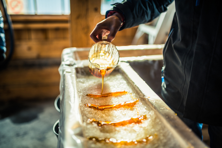 inside of a sugar shack showing a person pouring maple syrup over snow