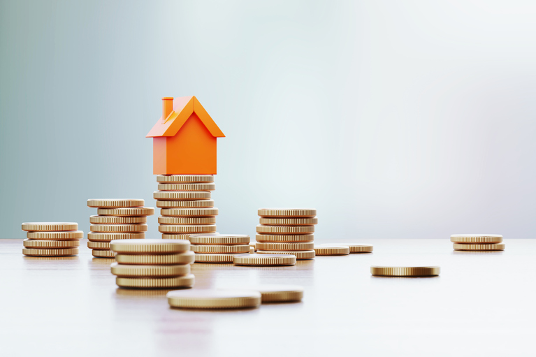 piles of coins with a little orange wooden house perched on one of the piles