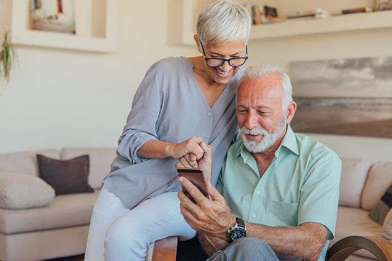 A man and a woman smiling and looking at the screen of a mobil phone.
