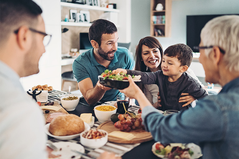 A family having dinner together, with a salad bowl being passed across the table.