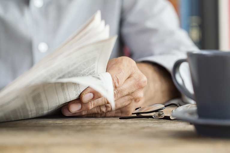 Man reading newspaper on table.