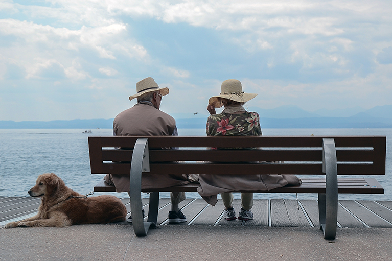 Two people sitting on on a bench. A dog is near them.