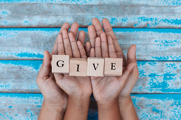 two hands holding 4 wooden letter spelling GIVE