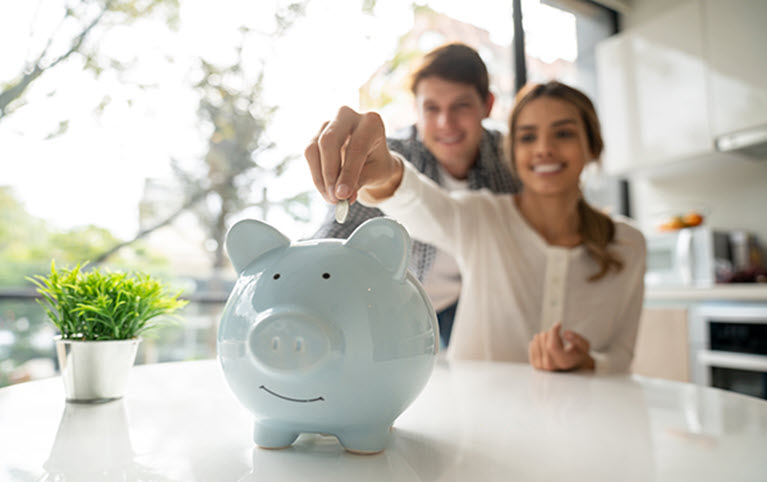 A couple and their piggy bank representing McMillan Goode Beer Wealth Advisory Group April 2023 newsletter. 