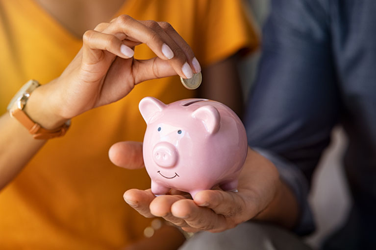 A hand placing a coin into a piggy bank.
