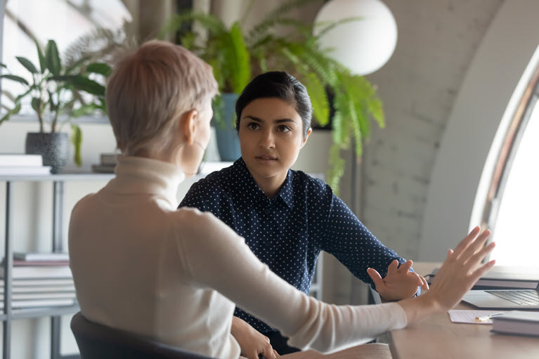 Two women seated in an office, speaking.