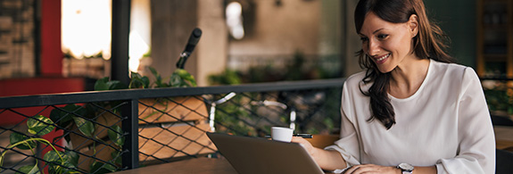 Women in a coffee shop looking at her investments on a laptop