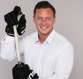 Alexey Manov (Jeff Wiebe Treasury Advisory Team) wearing black hockey gloves and holding a hockey stick vertically in front.