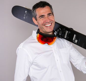 Jeff Wiebe (Jeff Wiebe Treasury Advisory Team) holding a black snowboard over one shoulder, with orange-tinted ski goggles hanging around his neck.