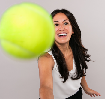 Danielle Bosaing (Jeff Wiebe Treasury Advisory Team) holding a tennis racket and hitting a bright yellow tennis ball that appears close to the camera. 