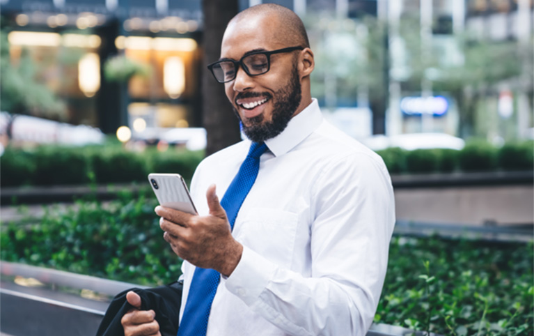 A man with glasses looking at his phone in the business district of a city