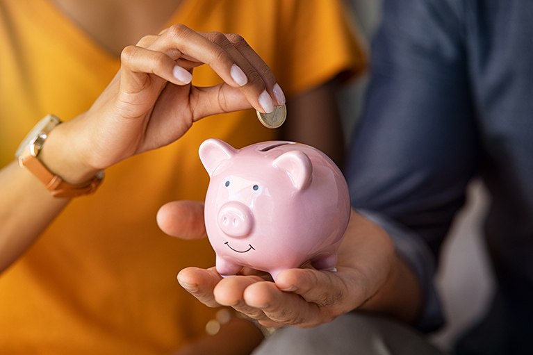 Close up of man holding pink piggybank while woman putting coin in it. Indian young couple saving money for their wedding. Close up of woman hand putting euro money in piggy bank to save for the purchase of an house.