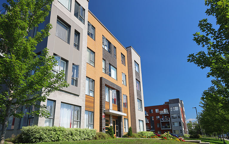 High rise condo building with smaller building in front with tress next to it.