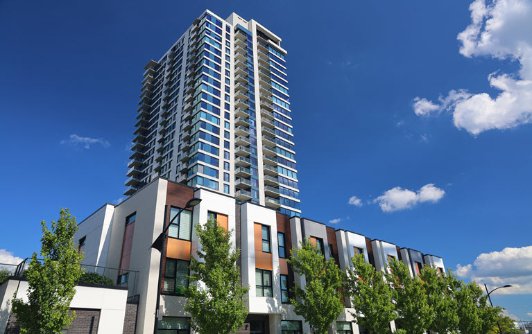 High rise condo building with smaller building in front with tress next to it.