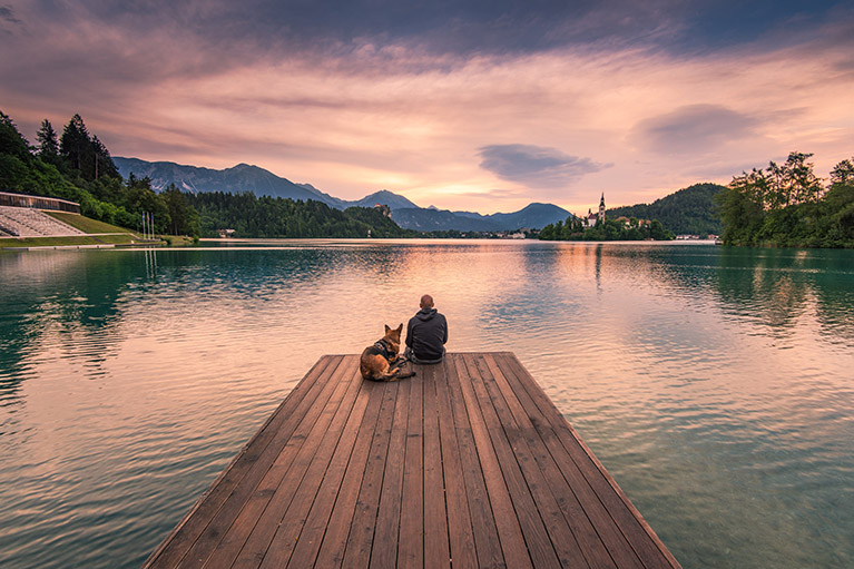 man and dog at the end of a dock with mountains
