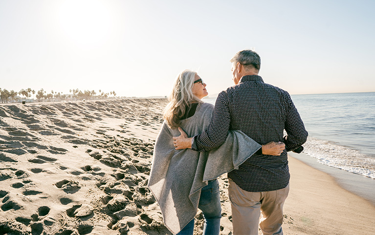 Image of an older couple who is walking by the beach discussing their upcoming retirement plans. 