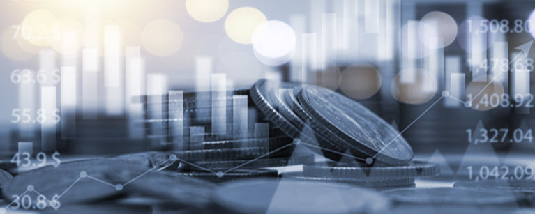 A stack of coins behind a grey blurred graph of stocks.