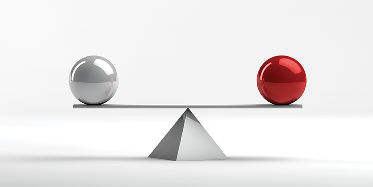 A metallic ball and a red metallic ball balanced on a pyramid.