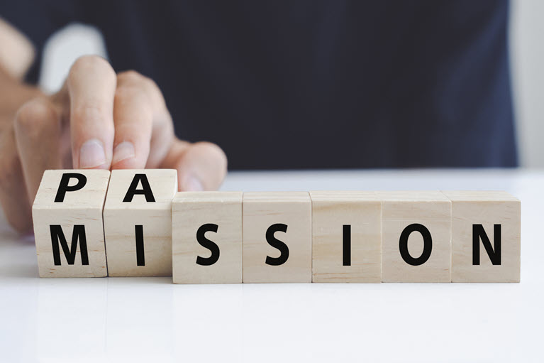 A man's hand turning a block of wood with the words passion and mission written on it.