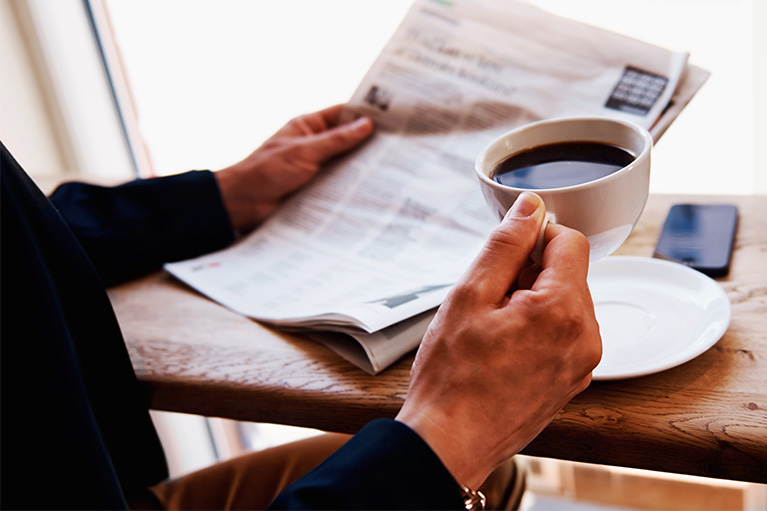 A man drinking a black coffee and reading a newspaper.
