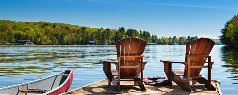 Two chairs on a dock facing a lake with a boat beside them.